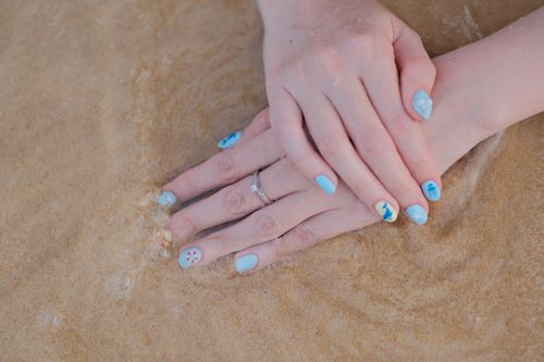 Free A serene close-up of hands with beach-themed nail art against sandy beach waves. Stock Photo