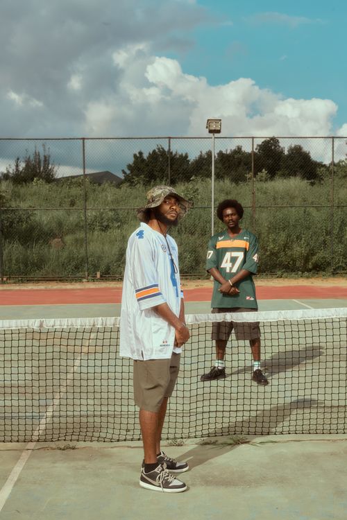 Free Two men in jerseys relax on an outdoor tennis court under a sunny sky. Stock Photo