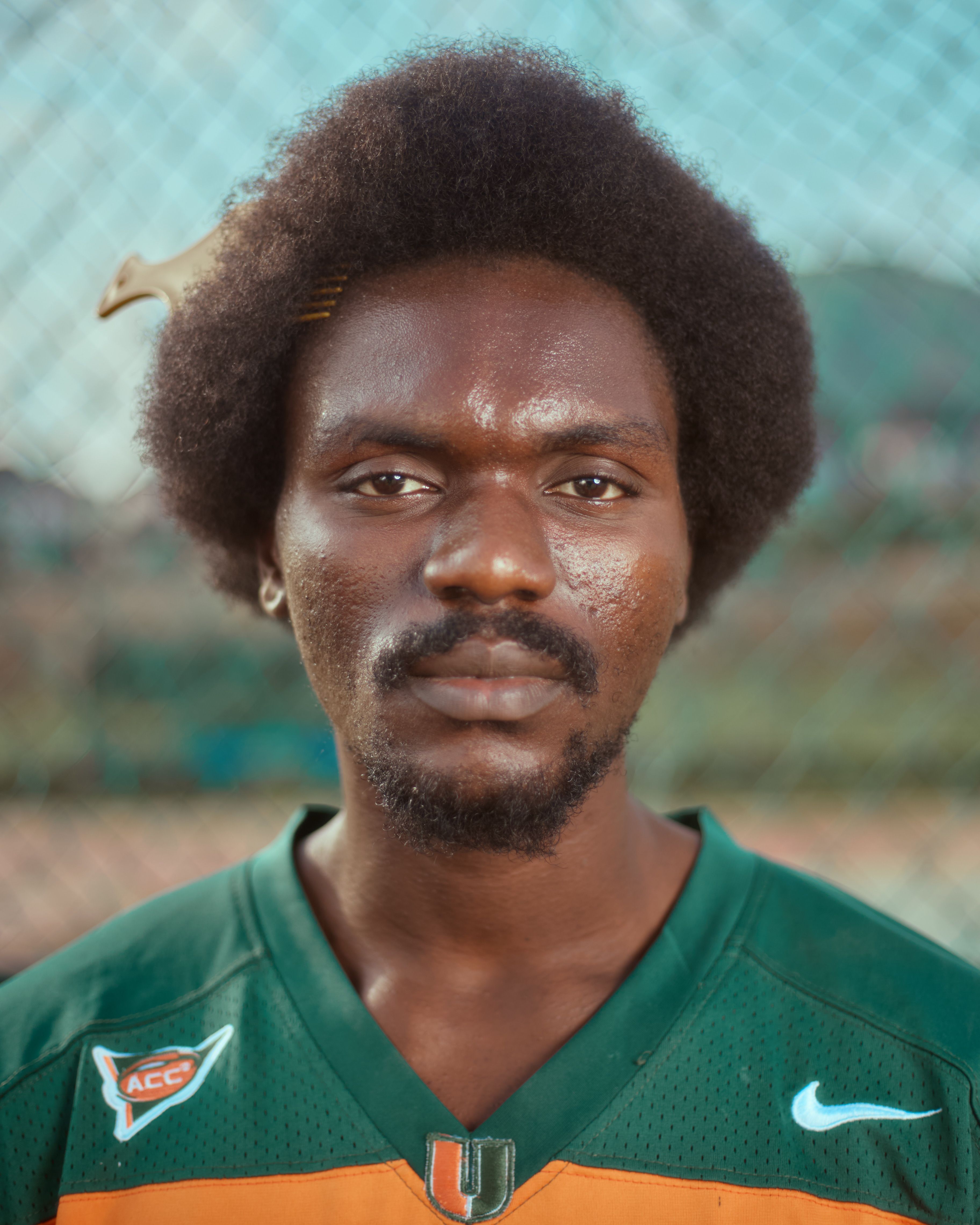 Close-up portrait of a young man wearing a green athletic jersey outdoors.