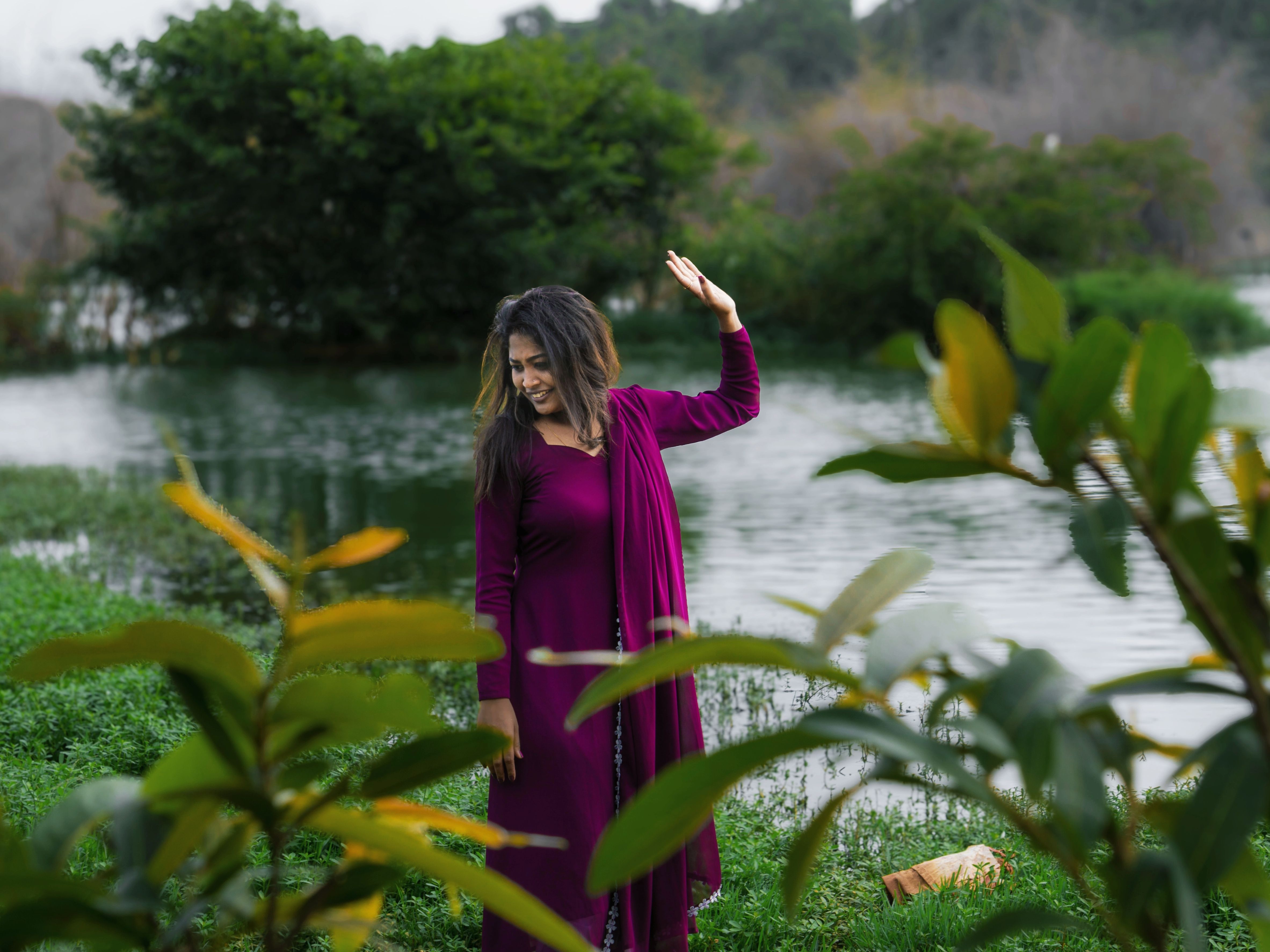 Woman in a vibrant magenta dress enjoying a tranquil moment by a lakeside with lush greenery.