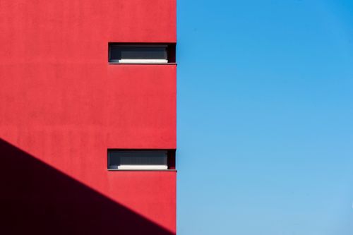 Free Minimalist photo of a red building facade with windows and shadow under a bright blue sky. Stock Photo