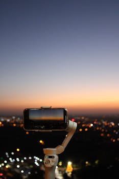 A smartphone mounted on a gimbal during twilight, filming a city skyline with vibrant lights.