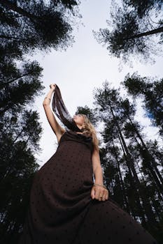 Fashionable woman in a stylish dress posing gracefully in a forest setting, showcasing elegance and nature.