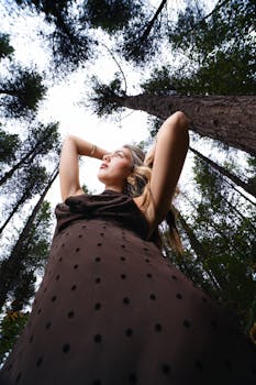 Elegant woman in the forest, captured from below, showcasing fashion and nature.