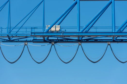 Close-up of a blue industrial crane against a clear blue sky, showcasing structure cables.