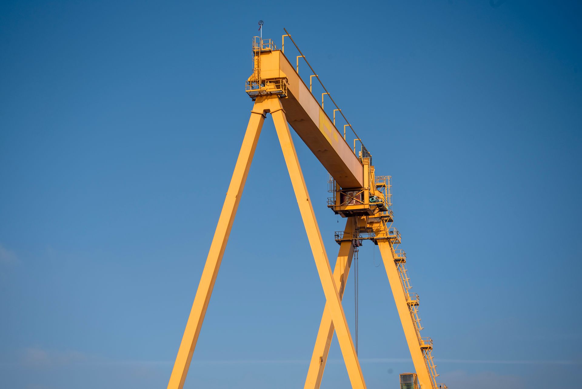 A large yellow crane stands tall against a clear blue sky, showcasing industrial strength.