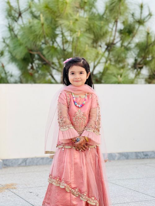 Free Portrait of a young girl in a pink traditional dress standing outdoors, smiling warmly. Stock Photo