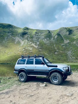 A rugged SUV parked beside a peaceful mountain lake under a clear blue sky.