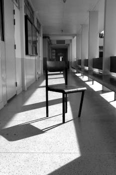 Black and white photo of a broken chair casting shadows in a school hallway.