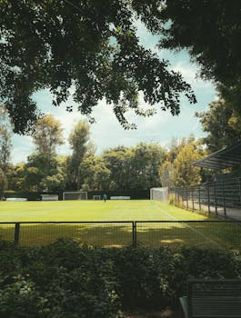 Photo by Santiago Sauceda González Serene view of an empty football field surrounded by greenery and trees on a sunny day.