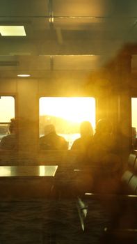 Passengers sit silhouetted against a vibrant sunset on a ferry ride.