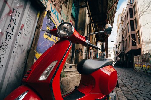 Free Urban red scooter parked on a graffiti-adorned corner, under a vintage structure. Stock Photo