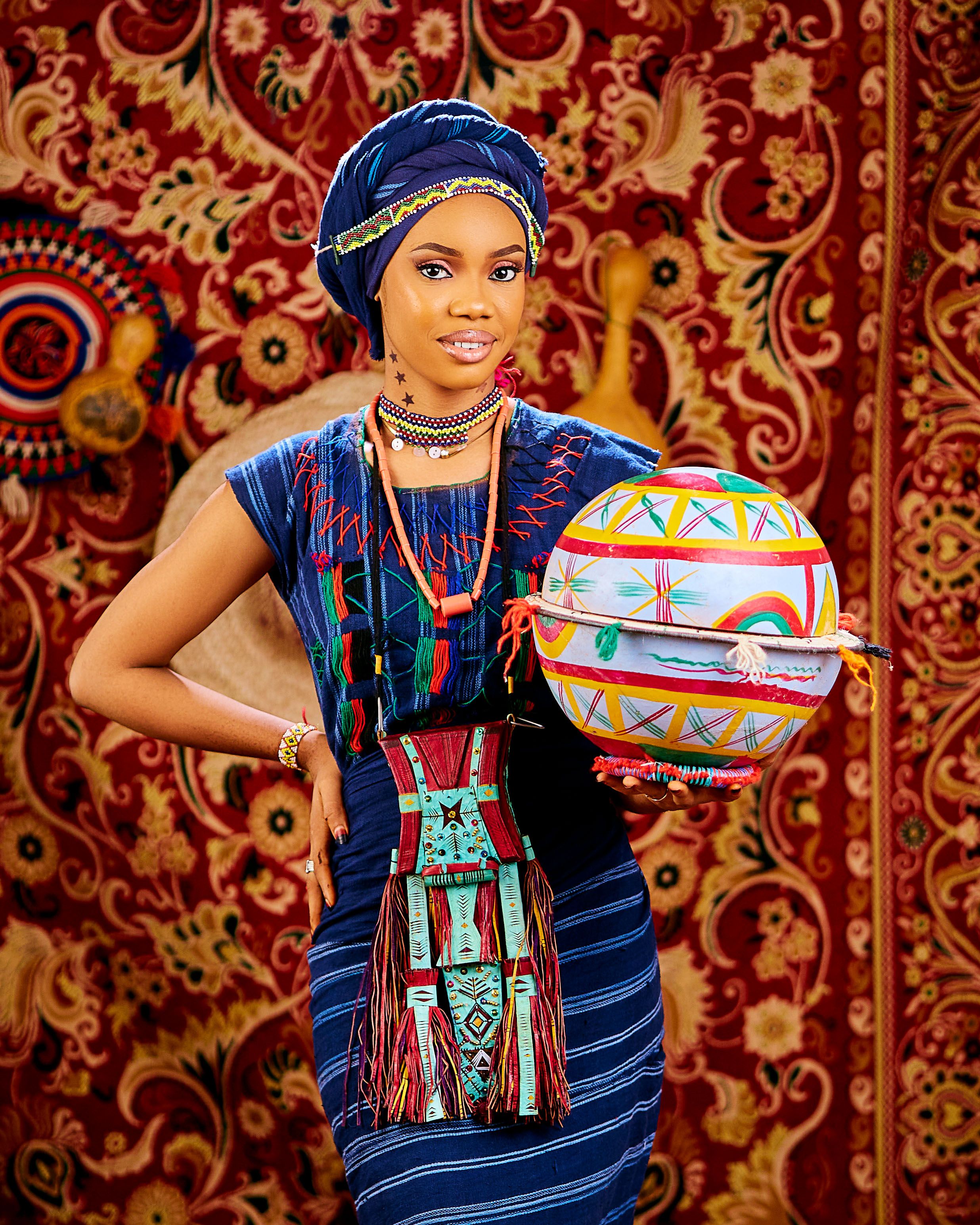 A woman in vibrant traditional African attire holding a woven basket with cultural patterns.