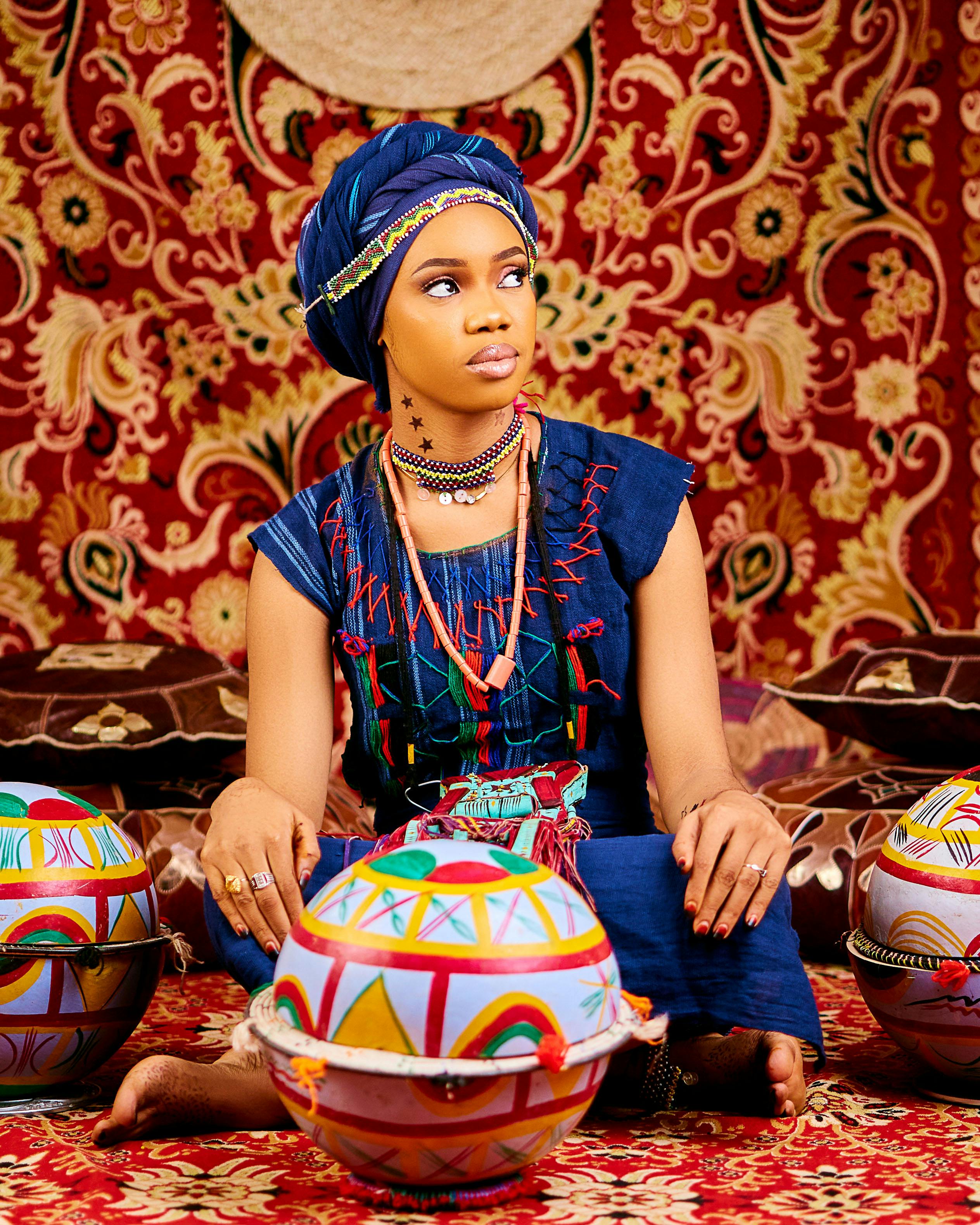 Vibrant portrait of a woman in traditional African clothing seated with colorful decorative elements.