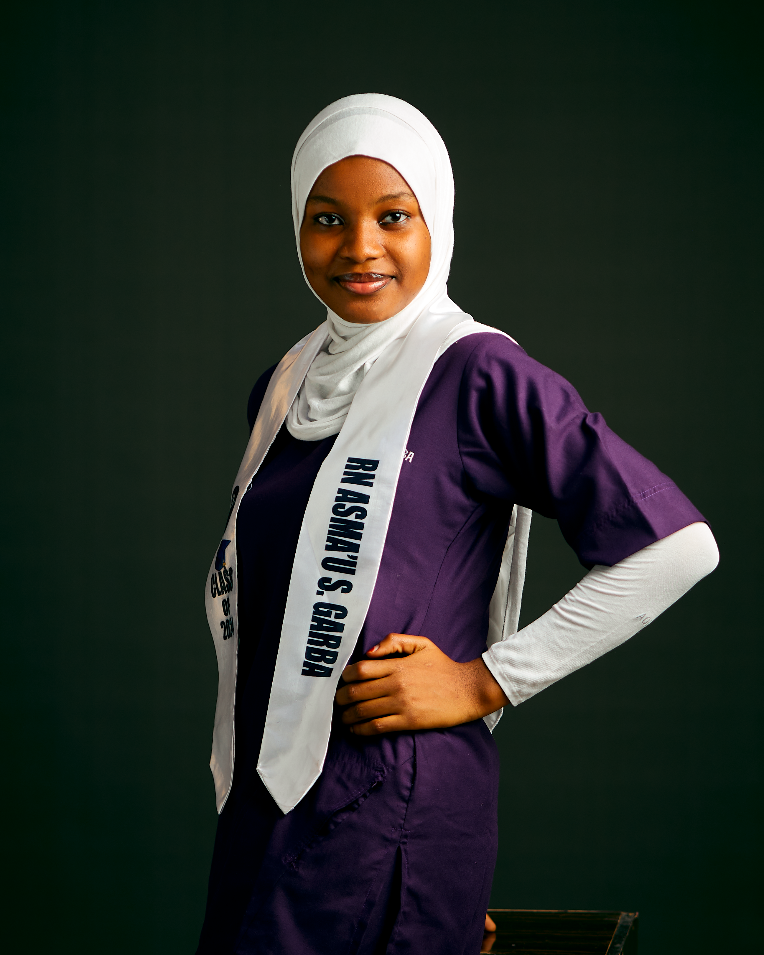Smiling young woman in a hijab poised against a dark background.