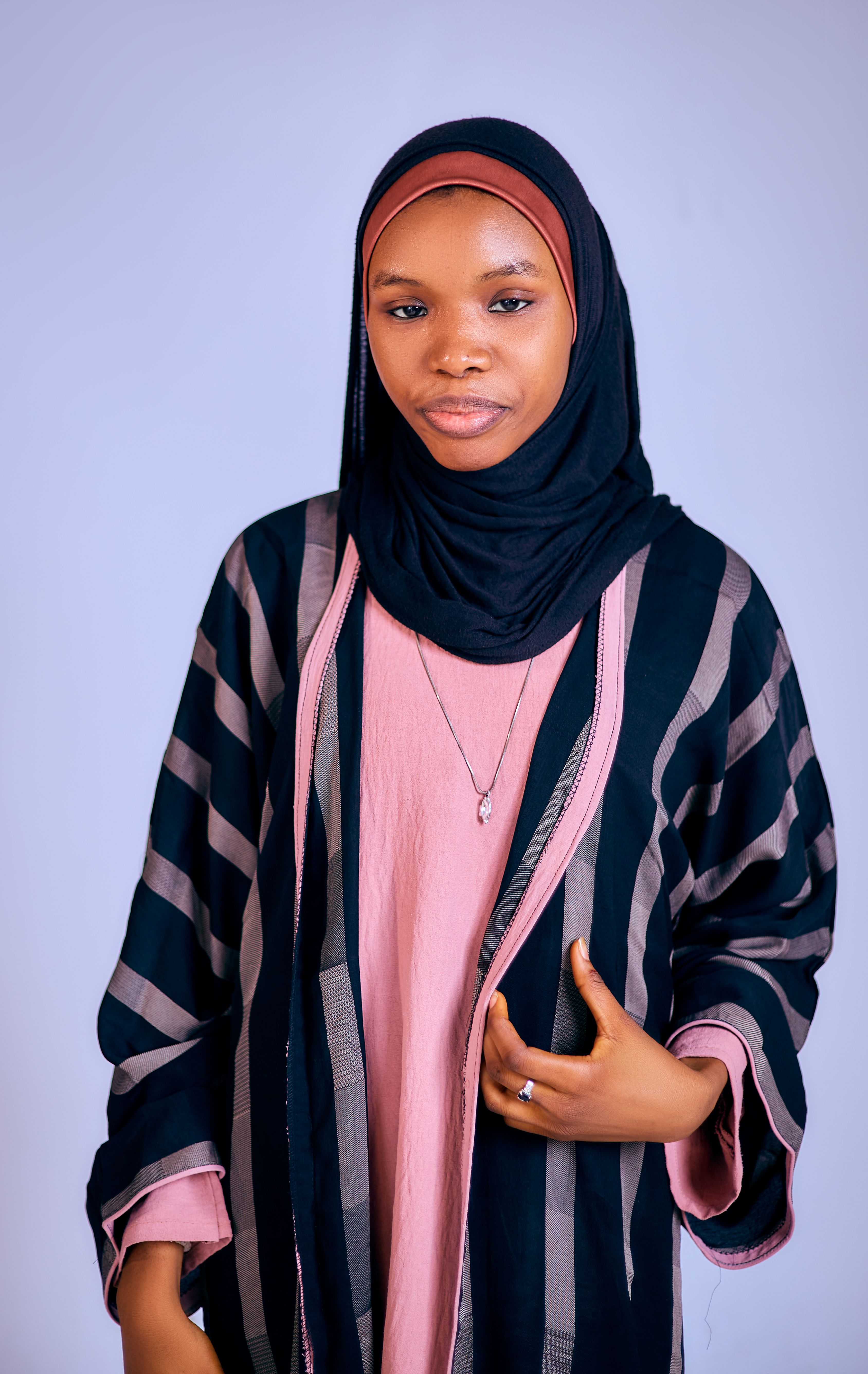 Young woman in a black hijab and striped abaya posing confidently.
