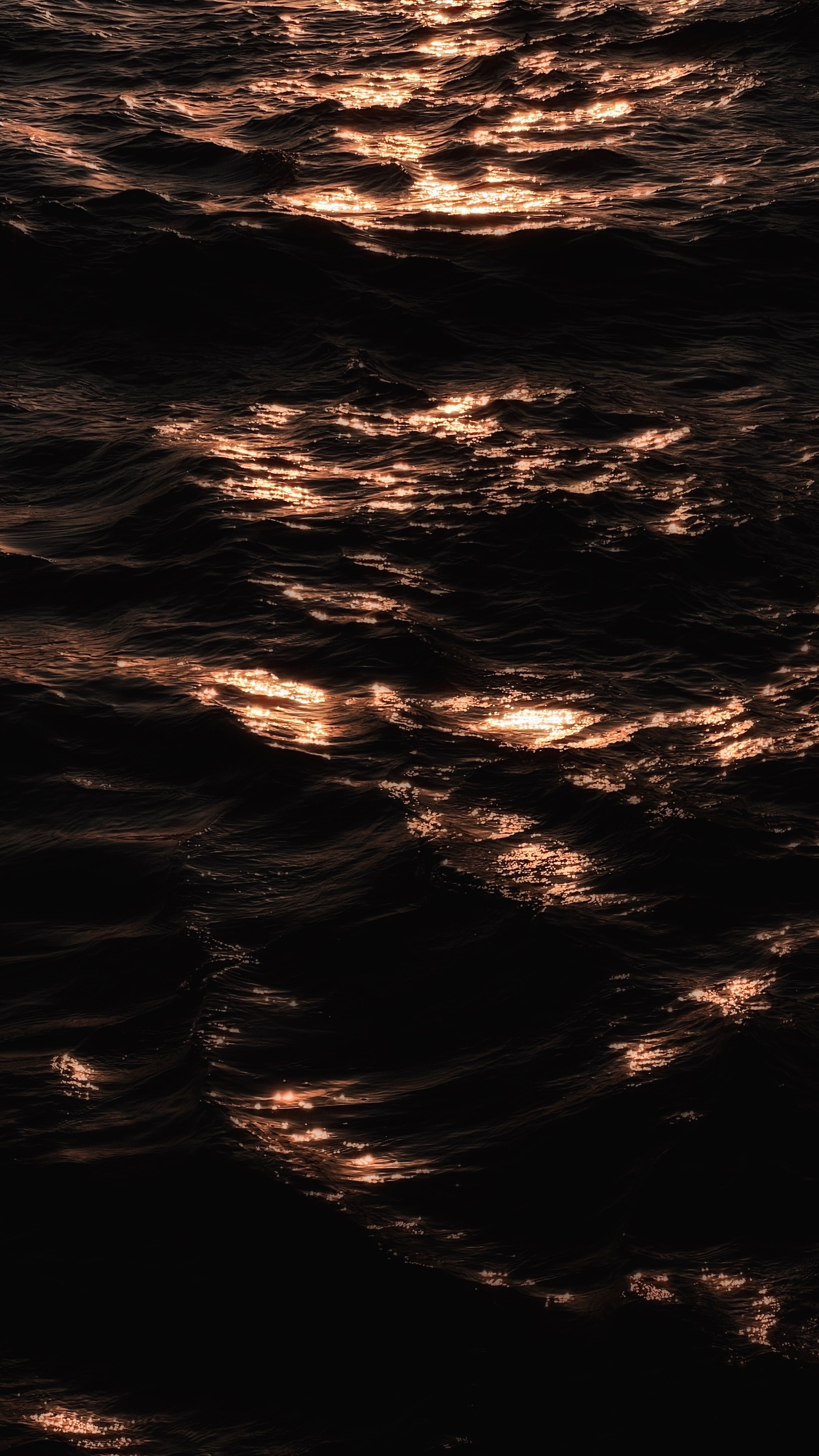 Golden sunset light reflecting on tranquil ocean waves, creating a serene and moody atmosphere.