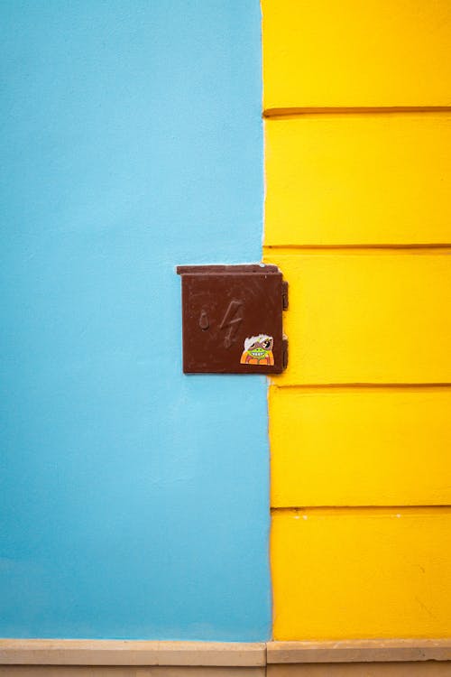 Безкоштовне Яскрава синьо-жовта стіна з центральною коричневою коробкою, що створює сміливий контраст. стокове фото