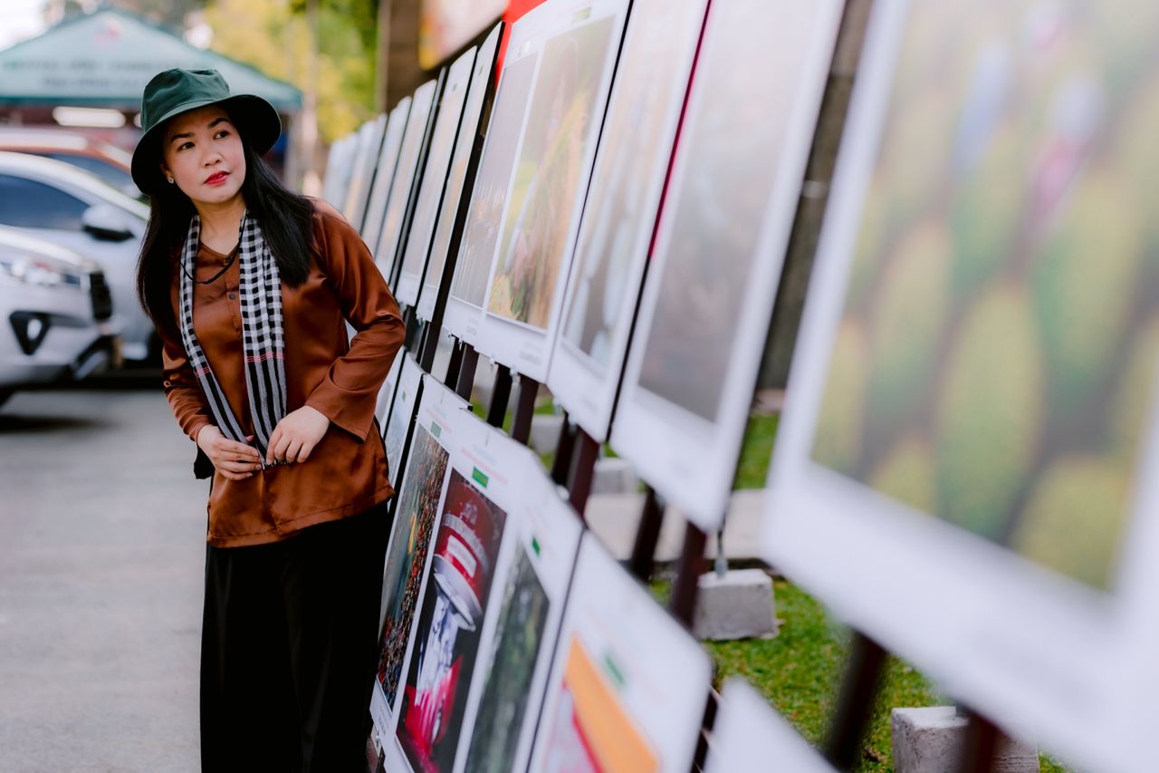 woman with hat viewing art at outdoor street exhibition surrounded by