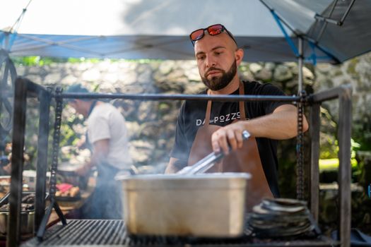Chef grilling food outdoors at an event with a focused expression.