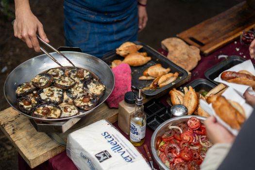 A vibrant outdoor BBQ scene featuring grilled mushrooms, fresh empanadas, and assorted salads.