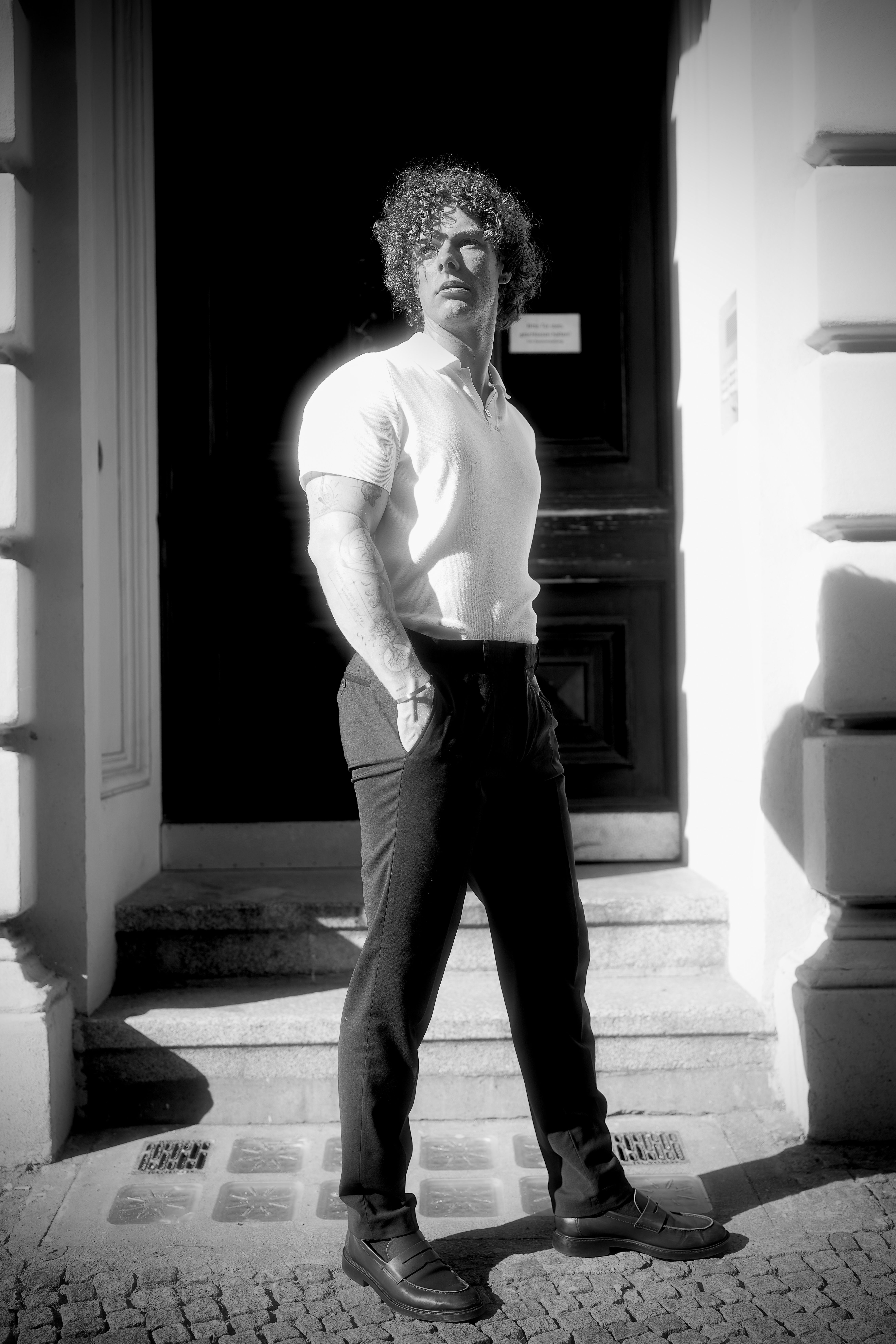 A black and white portrait of a man standing in front of a building in natural light.