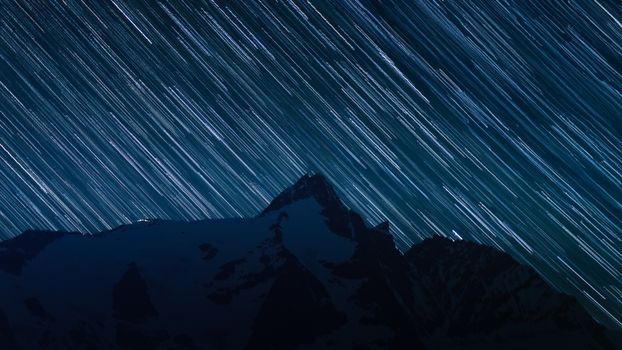 Captivating long exposure of star trails above snowy mountains, creating a cosmic nightscape.