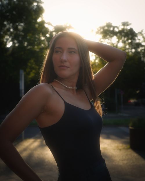 Free A stylish woman in a black dress poses outdoors with sunlight haloing her hair, creating a warm and serene ambiance. Stock Photo