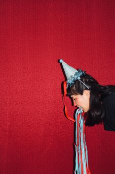 Woman with party hat spitting colorful streamers, red background, festive concept.