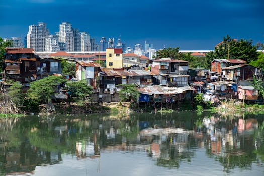 A stark contrast between slum dwellings and the modern city skyline across a reflective river.