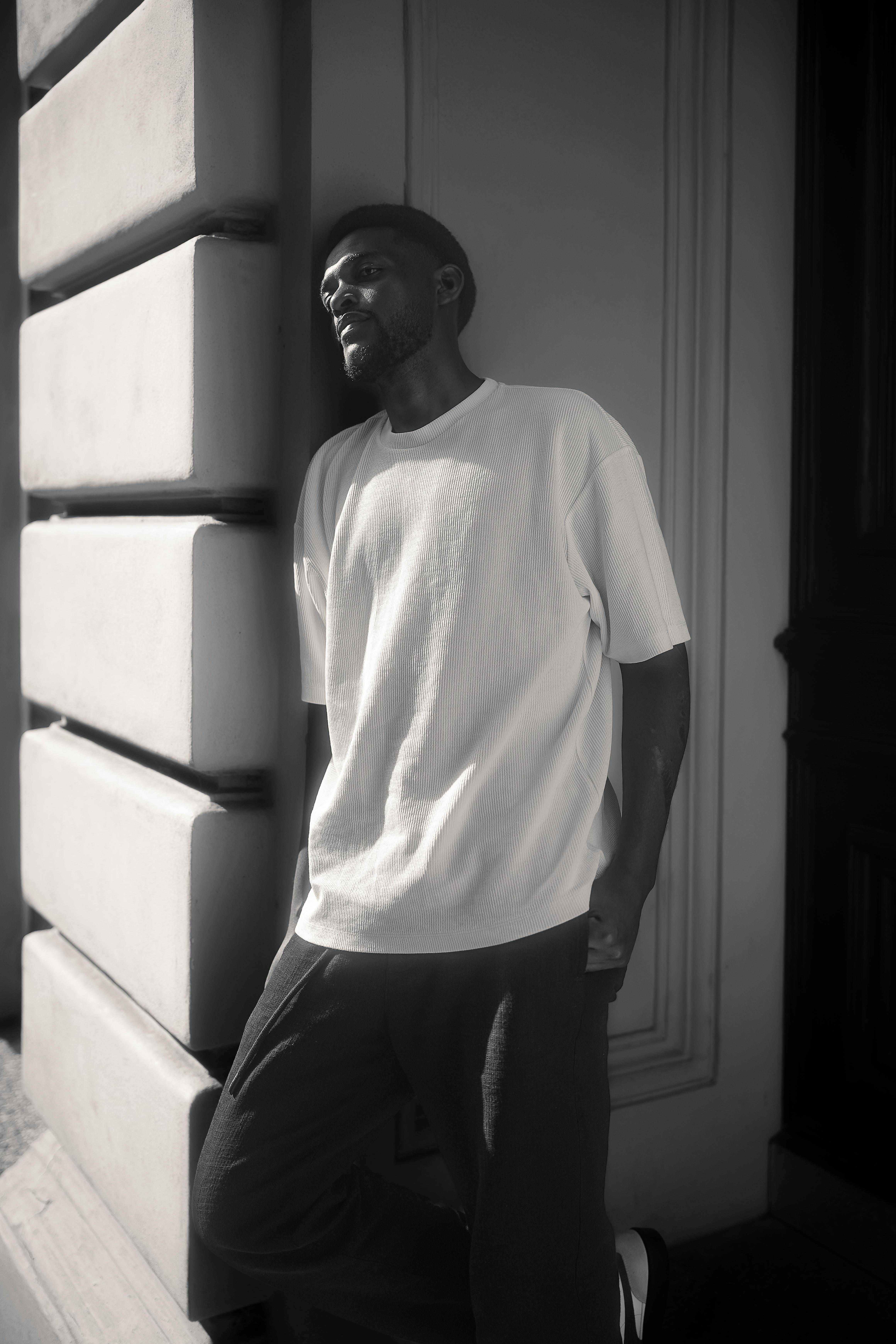 Black and white photo of a man leaning against a building wall, exuding a pensive mood.