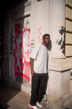 Man standing by graffiti art in Berlin, capturing street culture and sunlight shadows.