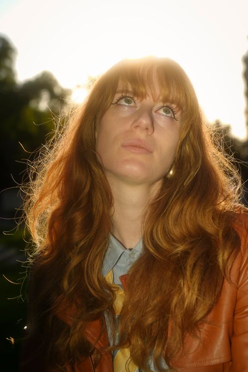 Free A woman with red hair gazing thoughtfully upwards in a sunlit outdoor setting. Stock Photo