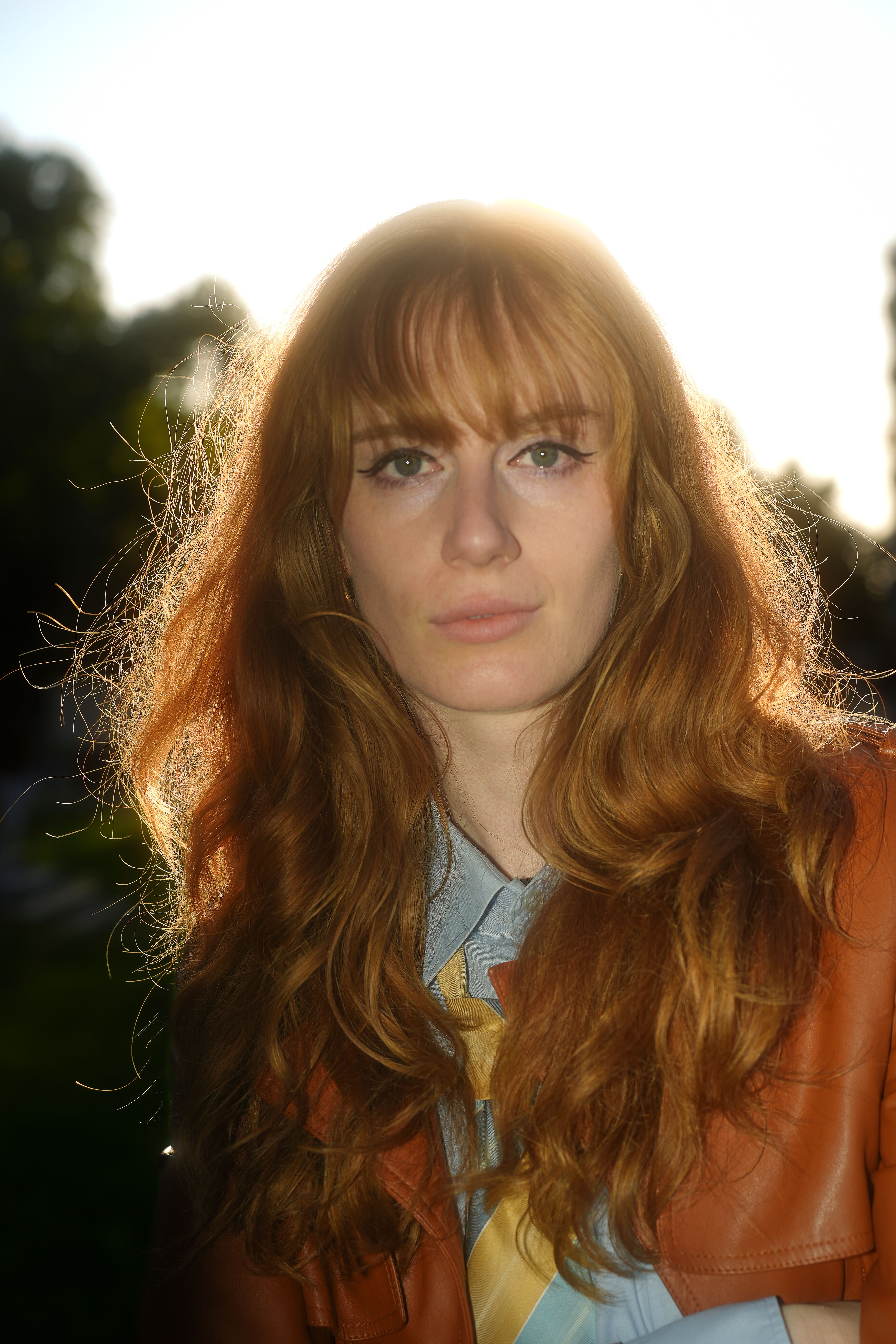 Outdoor portrait of a woman with striking red hair backlit by the sun during golden hour.