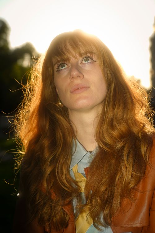 Free A young adult with red hair gazes upward, backlit by sunlight in an outdoor park setting. Stock Photo