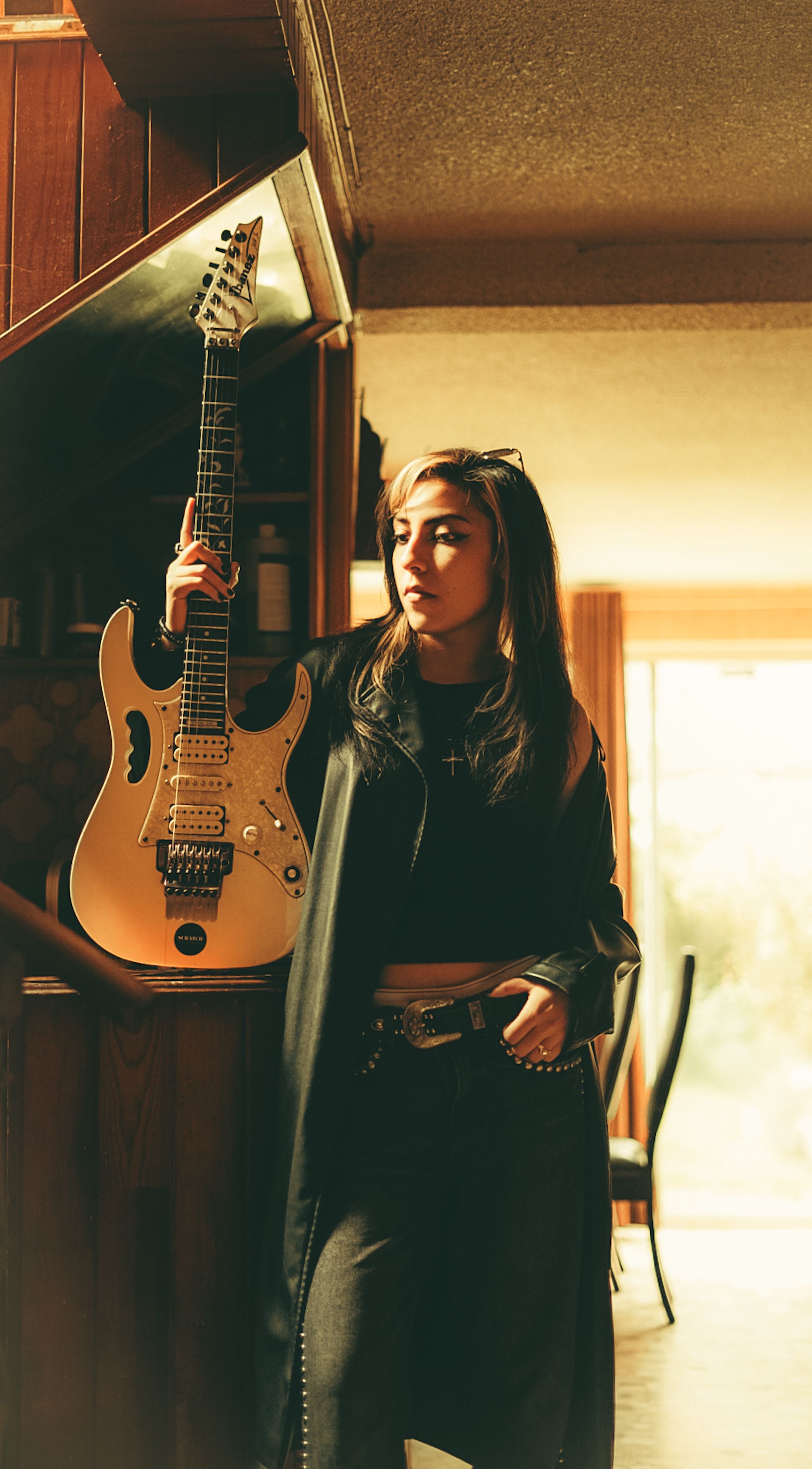 Stylish young woman posing indoors with an electric guitar, showcasing a rock music vibe.