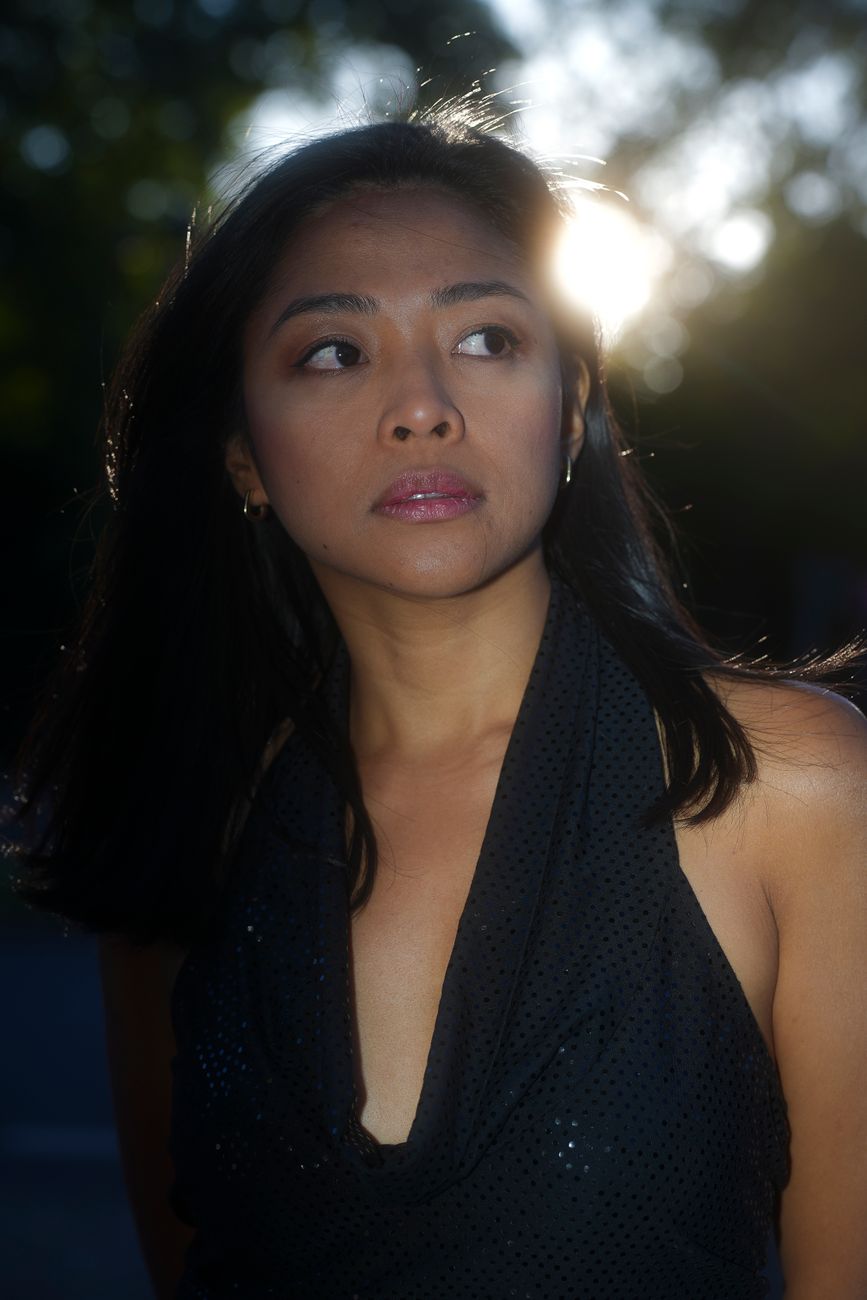 A thoughtful woman with long hair and a black dress, illuminated by the sunset.