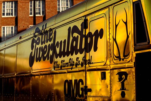 Close-up of a golden party bus featuring stylish typography and art in an urban setting.
