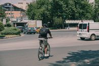 A cyclist rides through a city roundabout surrounded by vehicles and greenery, highlighting urban commuting.
