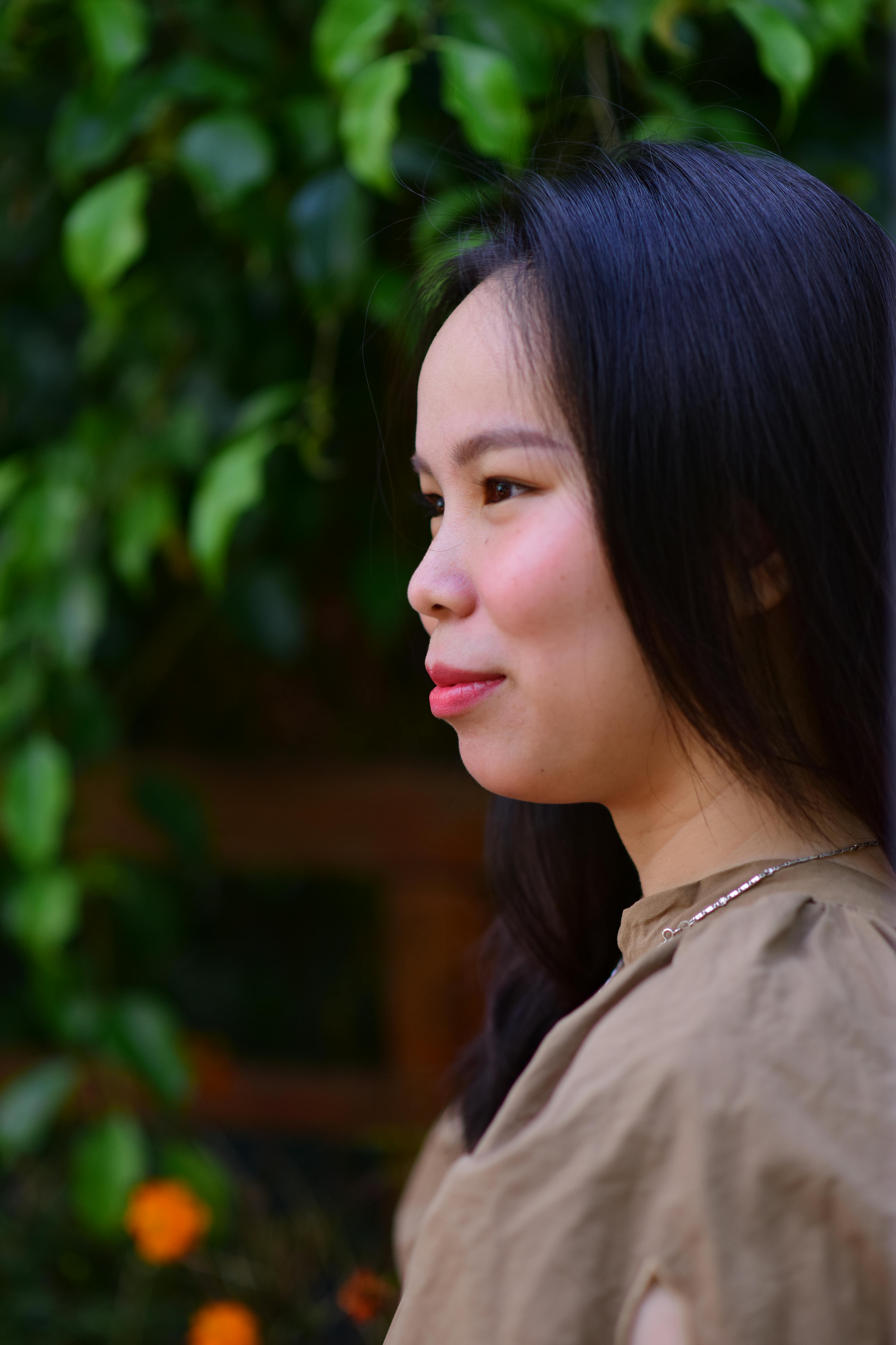 Side profile portrait of a woman with long dark hair, set against green foliage, exuding a serene and natural vibe.