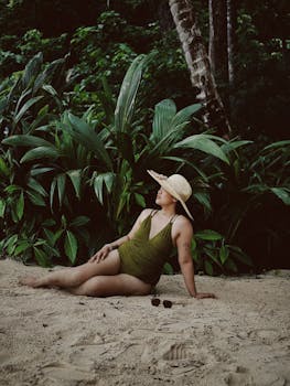 Woman in a straw hat lounging on a tropical beach, surrounded by lush greenery.