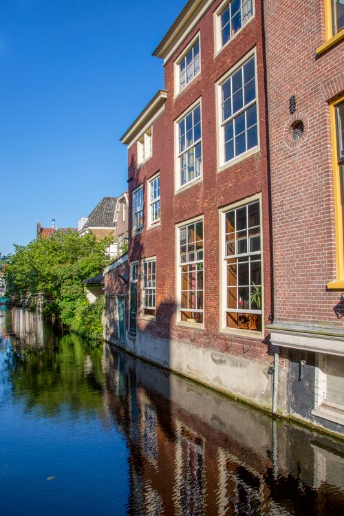 Free Charming red brick building reflecting in a canal, under blue skies, capturing quintessential Dutch architecture. Stock Photo