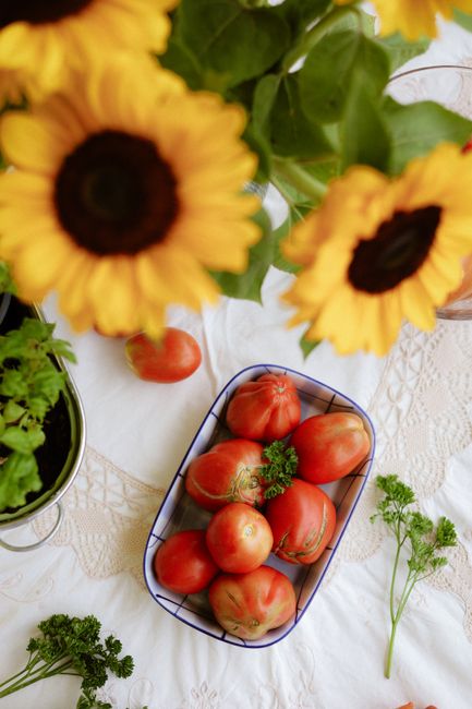 Bright arrangement of sunflowers and fresh heirloom tomatoes on a table.
