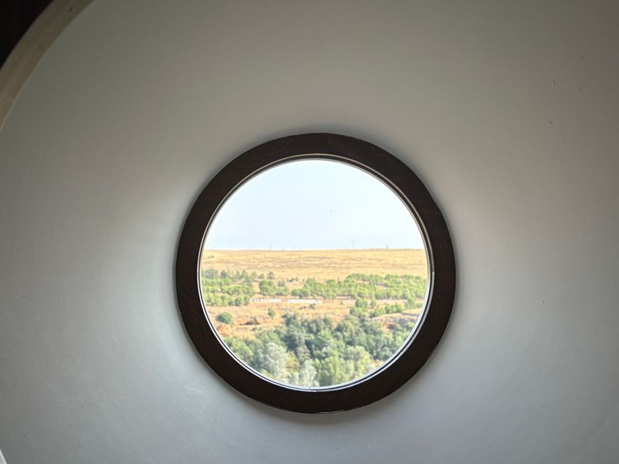 A scenic view of Segovia's landscape through a circular window, showcasing lush greenery and fields.