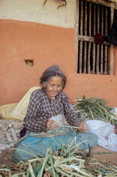 An elderly woman sitting outside preparing vegetables, showcasing traditional rural life.