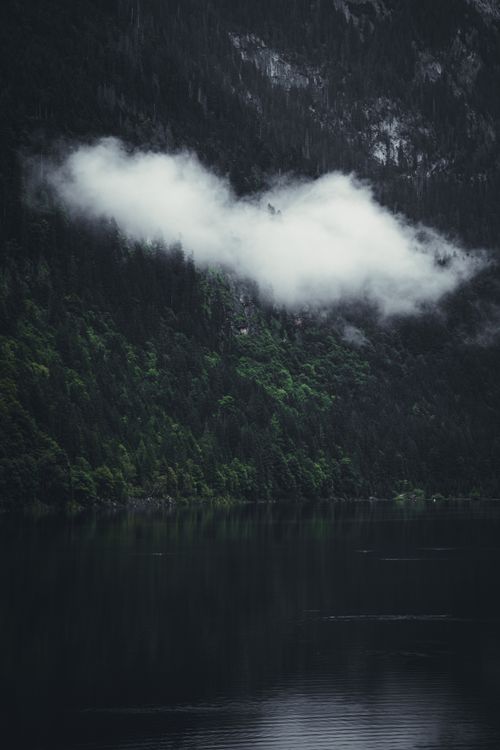 Free Dramatic view of clouds over a dense forest reflecting on a serene lake. Stock Photo