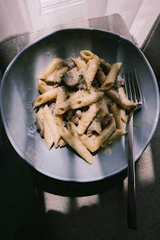 Black and white photo of creamy mushroom pasta in a blue bowl with a fork.