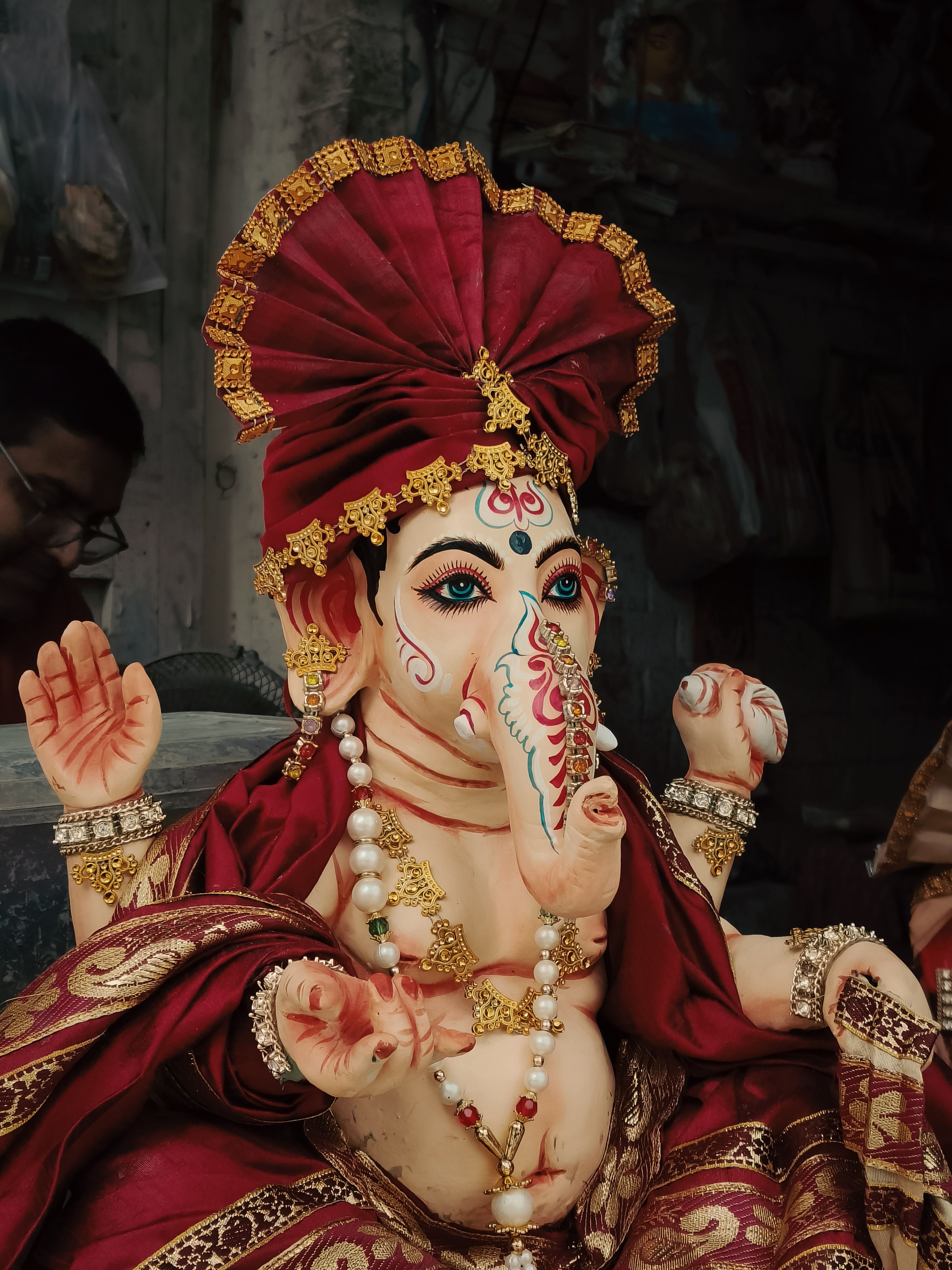 A detailed Ganesh idol with vibrant colors and intricate decorations in an artisan's workshop.