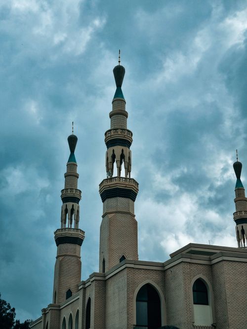 Free A beautiful view of mosque minarets reaching towards a dramatic cloudy sky, showcasing Islamic architecture. Stock Photo