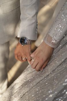 Elegant close-up of a couple holding hands in wedding attire, showcasing rings and watch.